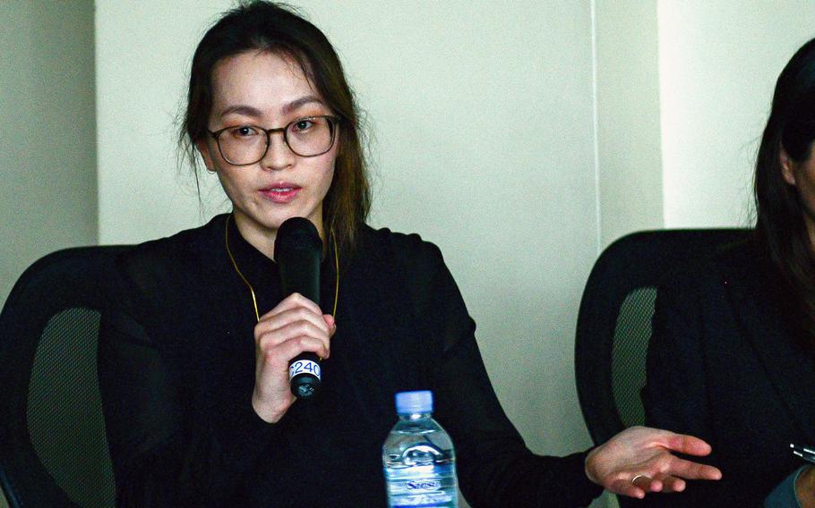A woman in a black shirt gestures as she speaks into a microphone.
