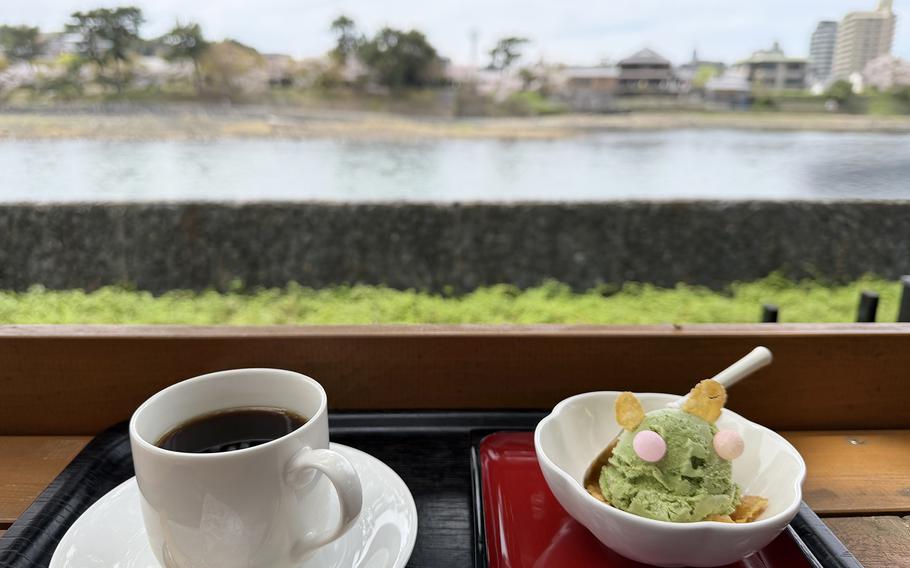 A cup of coffee and a bowl of green ice cream sit on a tray overlooking a river.