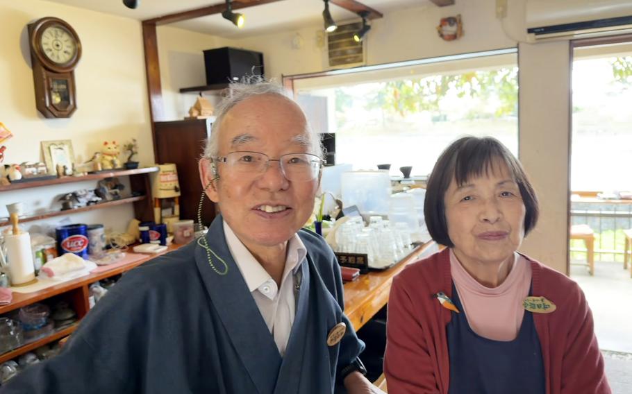An elderly man and woman pose in a cafe.