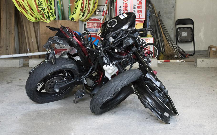 A badly damaged motorcycle is pictured in front of signs on Okinawa.
