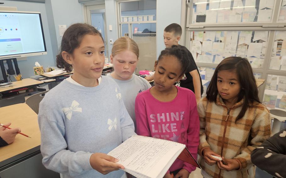 A group of grade schoolers stand together in a classroom looking at notes.