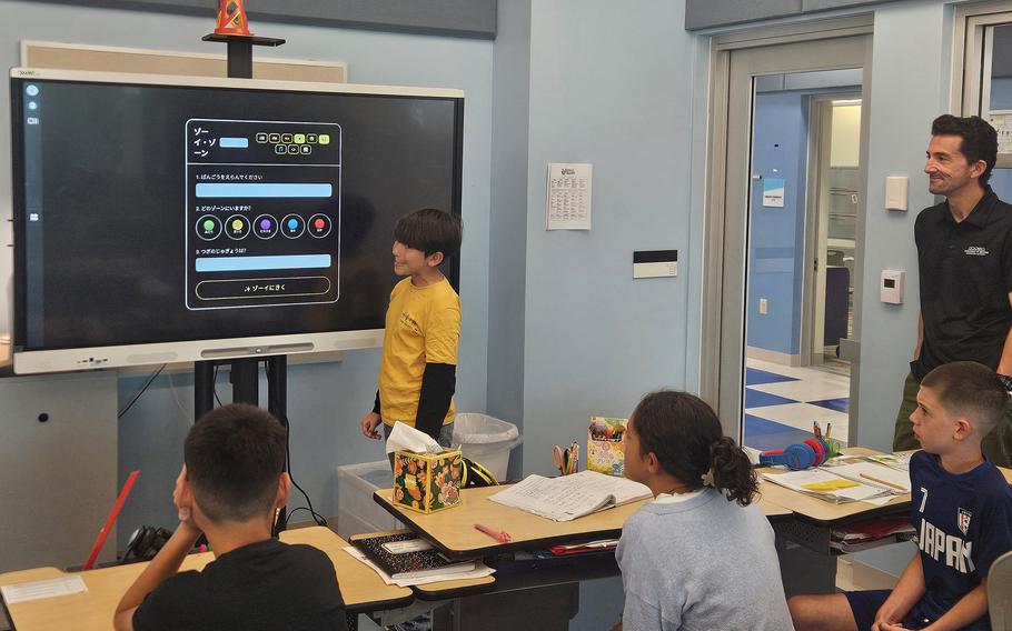 A gradeschool boy stands to present a project in front of the class.