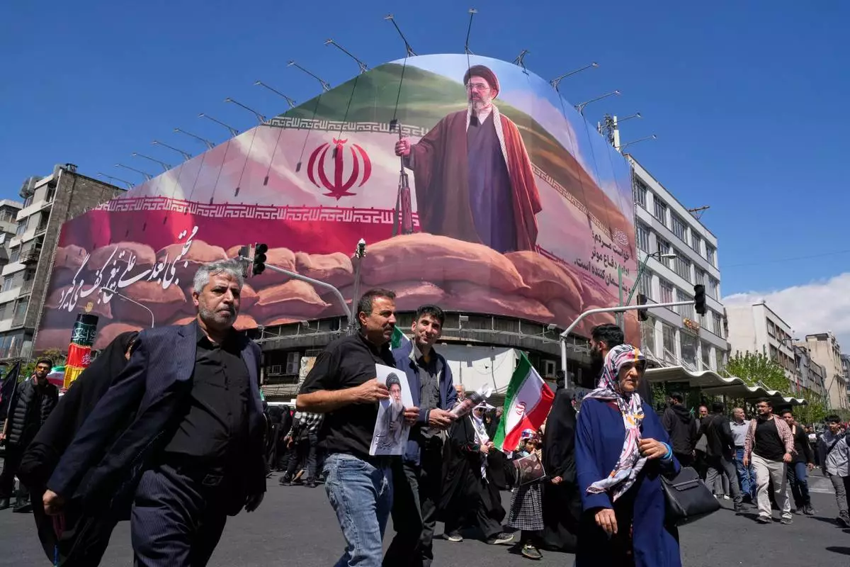 Government supporters walk past a billboard depicting Iran's Supreme Leader Mojtaba Khamenei as they gather to mark the 40th day since the killing of his father, slain Supreme Leader Ayatollah Ali Khamenei, in Tehran, Iran, Thursday, April 9, 2026. (AP Photo/Vahid Salemi)