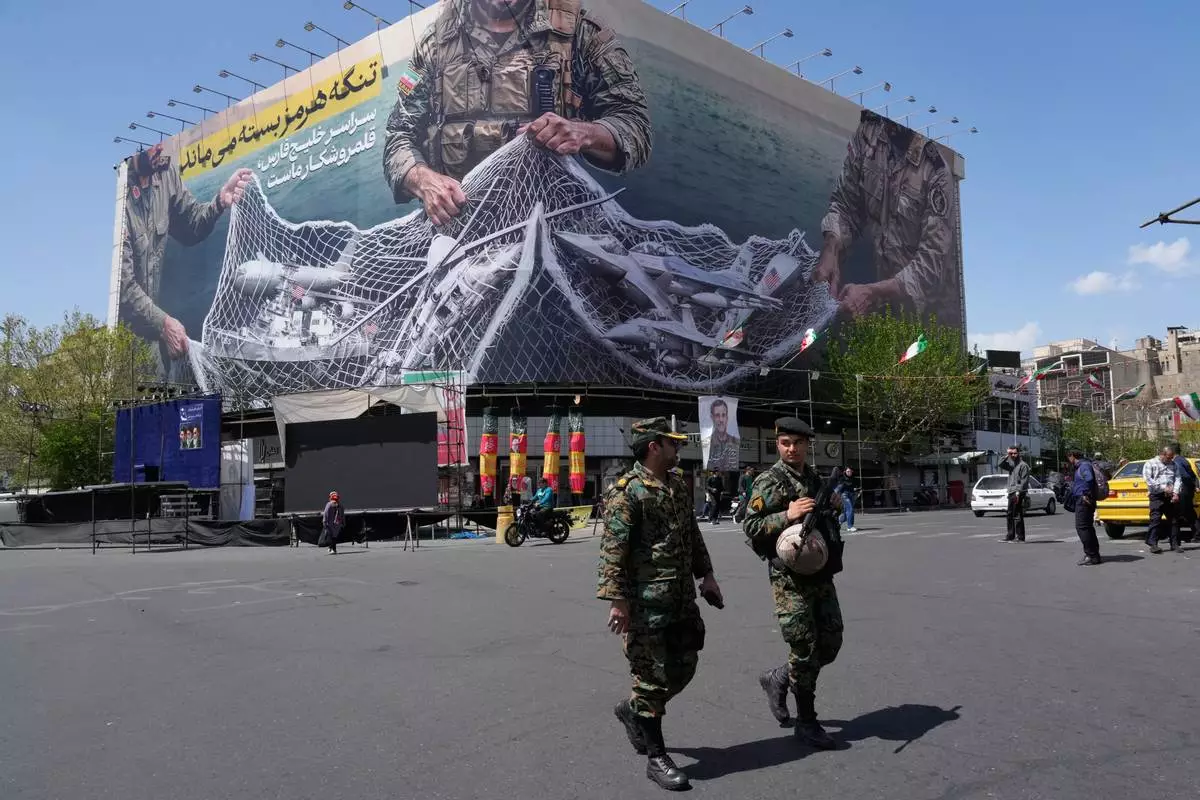 FILE - Two police officers walk in front of an anti-U.S. billboard depicting American aircraft being caught by Iranian armed forces in a fishing net beneath the words in Farsi, "The Strait of Hormuz will remain closed, The entire Persian Gulf is our hunting ground," in Tehran, Iran, Sunday, April 5, 2026. (AP Photo/Vahid Salemi, File)