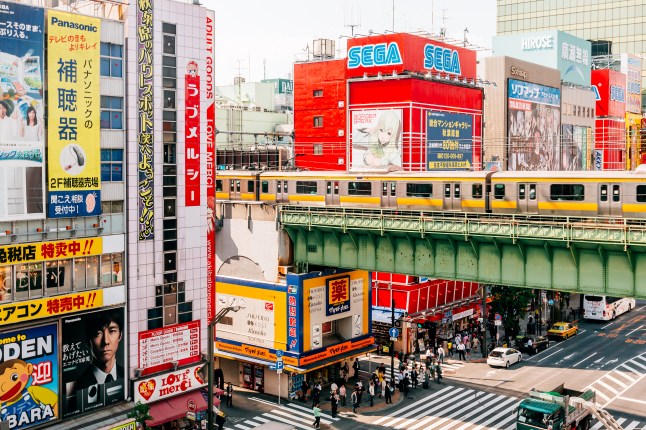 A view of the colourful Akihabara district in Tokyo, Japan, with a train going over a railway bridge next to bright shops covered in large advertisements.