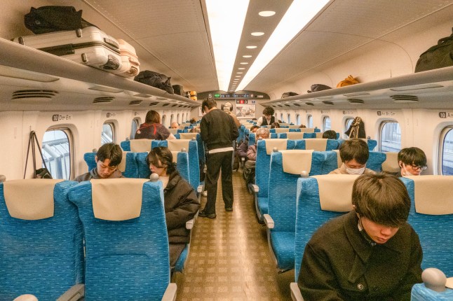 Passengers sitting on seats inside the carriage of a Shinkansen high-speed train in Japan.