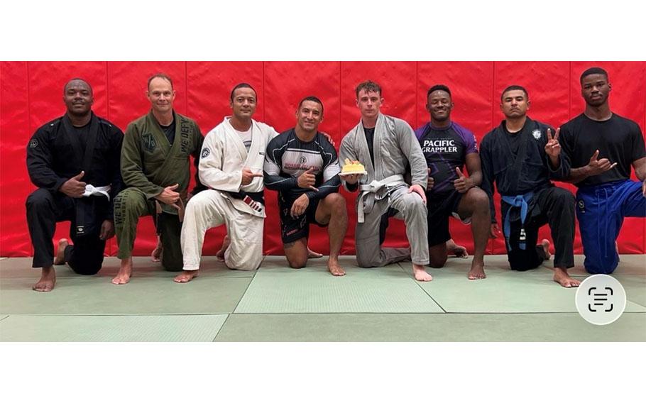 8 jiu jitsu players pose for a photo on tatami mats.