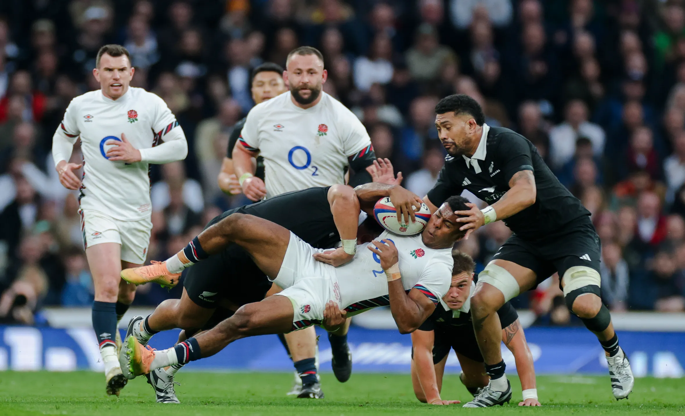 Immanuel Feyi-Waboso of England is tackled by Asafo Aumua of New Zealand during a rugby match.