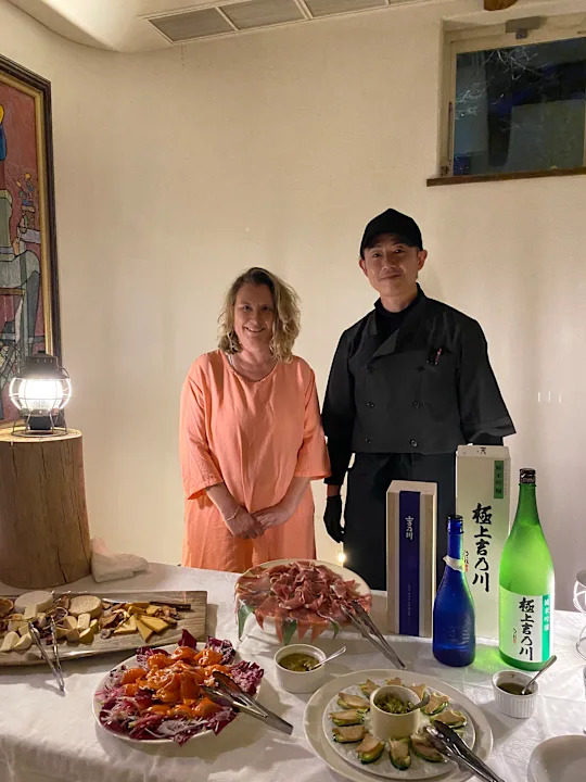 Woman and chef stood in front of Japanese food and bottle of saki