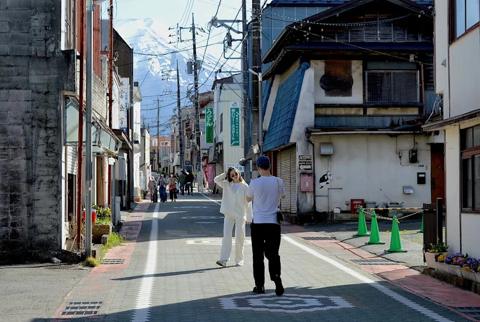 Tourists snap a picture in a rural Japanese street, with Fuji as a one-of-a-kind backdrop.