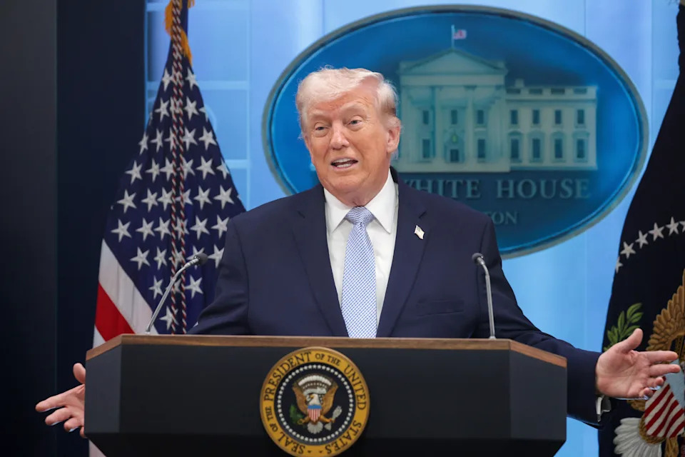 A person speaking at a podium with the White House emblem in the background, flanked by American flags