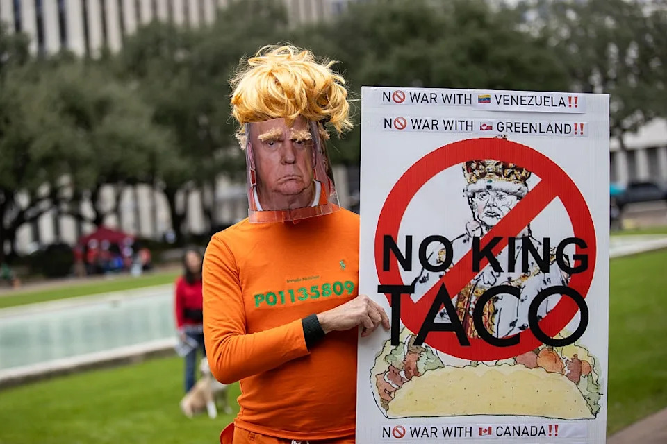 Protester in a mask and wig holds a sign against Taco Bell, referencing U.S. politics, at a demonstration