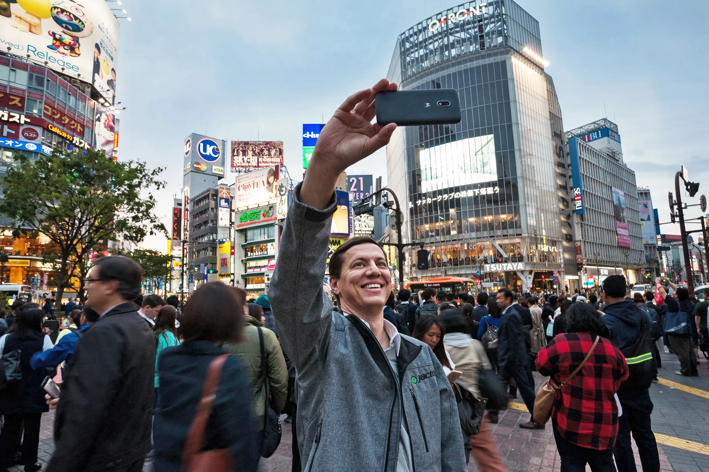 A tourist taking a selfie with a smartphone at Shibuya Crossing in Tokyo.