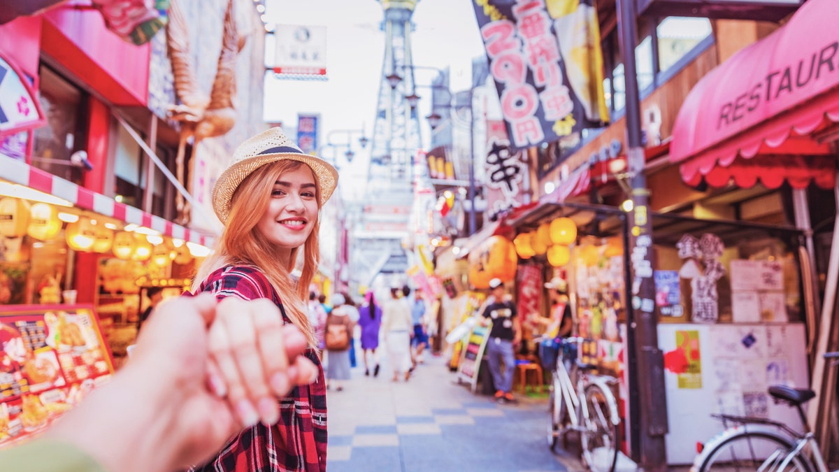Young attractive female holding boyfriend's hand walking in Shinsekai market streets Osaka Japan