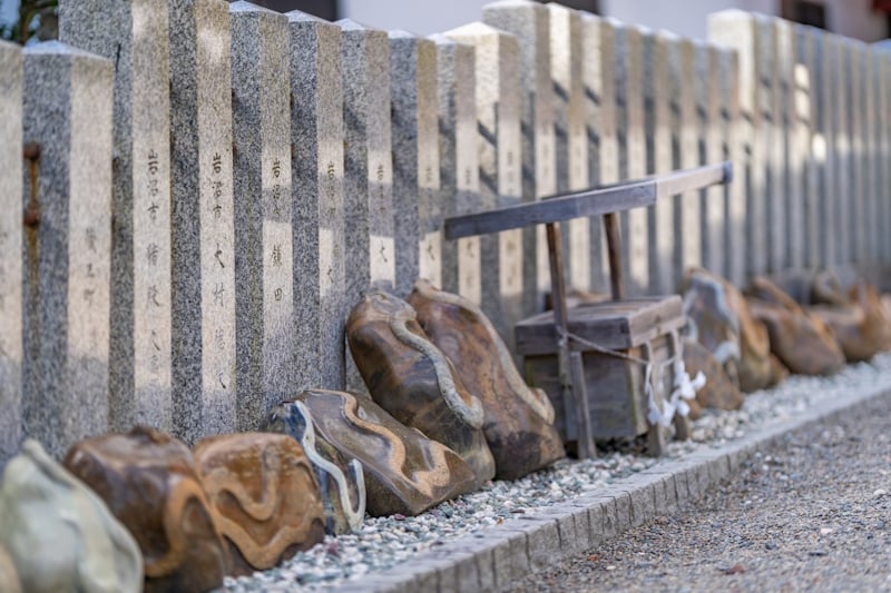 Snake-patterned stones arranged in front of a donor stone fence at Kanahebisui Shrine