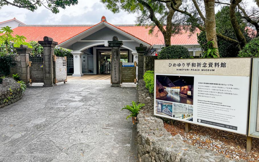 A museum exterior shows a sign and an entrance with a white building with a red roof.