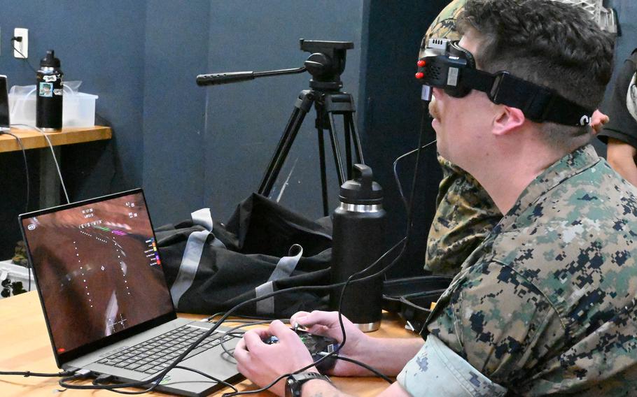 A Marine wears a headset and sits in front of a computer while using a drone simulator.