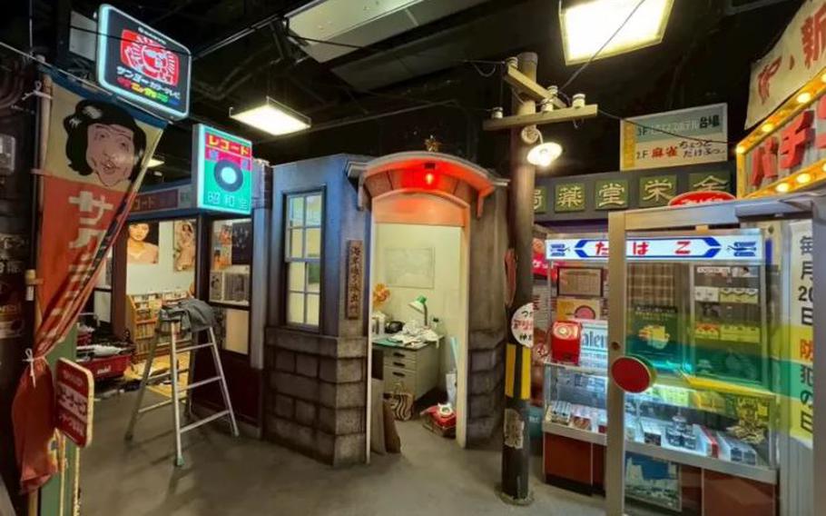 A street in the Showa era. A police box, a tobacco store, and some other stores are visible.