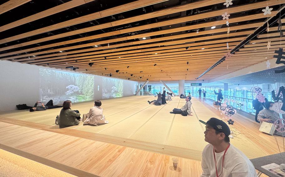 A room with people sitting on tatami mats is reflected in a wall-length mirror.