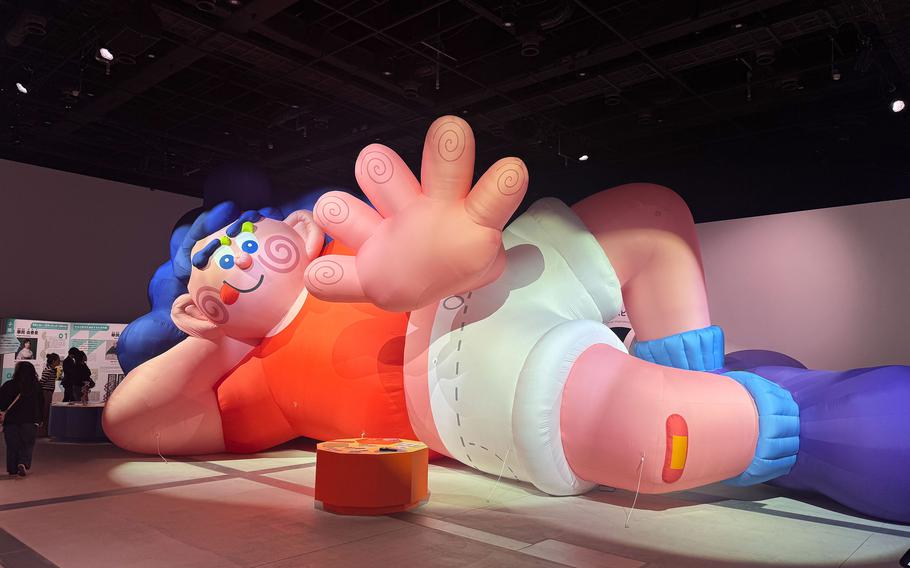 A large inflatable figure reclines on the floor and waves hello.