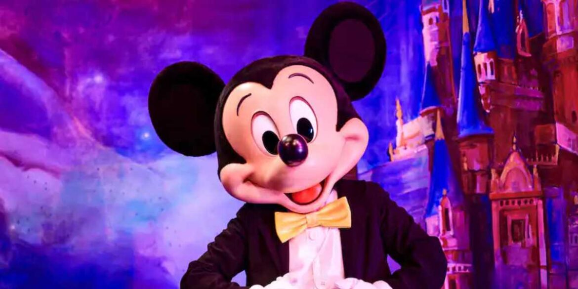 Disney World Travelers Suddenly Get Unexpected Flight News as Massive Japan Vacation Deal Emerges Mickey Mouse in a tuxedo with a yellow bow tie stands smiling before a colorful, magical backdrop featuring the iconic castle at Shanghai Disney Resort.