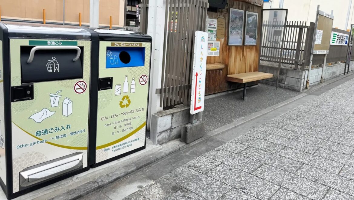In bin-scarce Kyoto, solar trash cans crush waste and signal crews before they overflow Two bins for waste disposal beside a wooden bench at a bus stop.