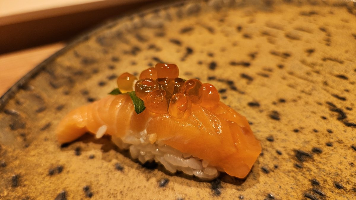 A slice of pink salmon draped over a finger of rice and topped with salmon roe