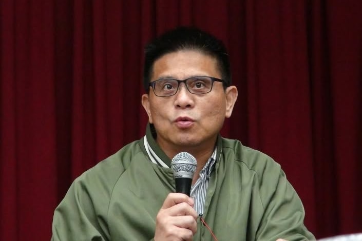 Dr Awi Mona, mid speech, holding a microphone.