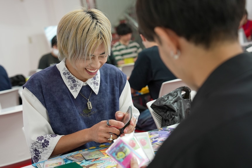 Two people, one visibly laughing, sitting across each other with cards laid out between them