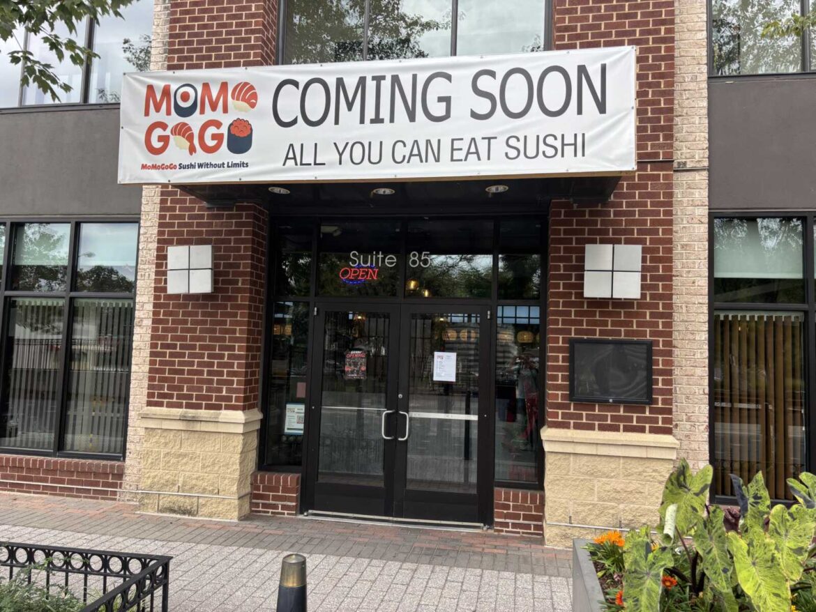 New all-you-can-eat sushi restaurant opens in Penrose Square Restaurant storefront with a large ‘Coming Soon’ banner for Momogo Sushi, entry doors under a brick facade, suite 85 signage visible
