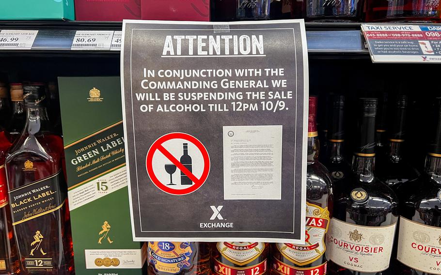 A sign posted in the liquor section of an Army & Air Force Exchange Service store announces a temporary suspension of alcohol sales until noon on Oct. 9. The notice is displayed among shelves stocked with whiskey, cognac and other spirits, and includes a red prohibition symbol over a wine glass and bottle.